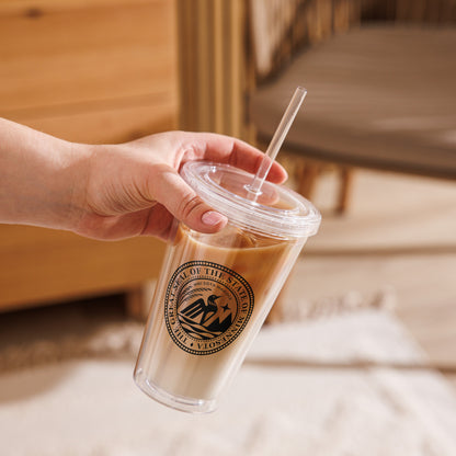 Hand holding a clear cup with a straw, featuring the Minnesota State Seal, against a blurred indoor background.