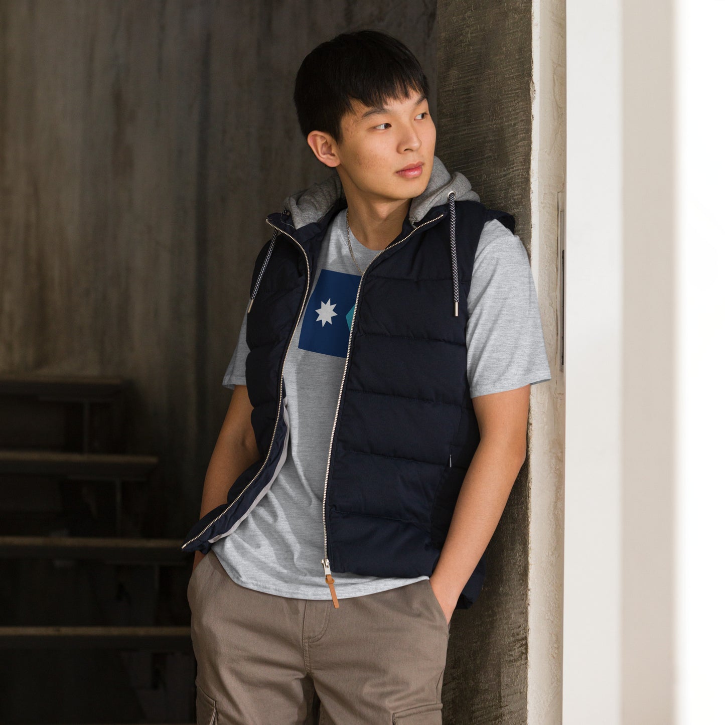 Person wearing a navy puffer vest over a gray shirt featuring the Minnesota State Flag, standing against a neutral wall.